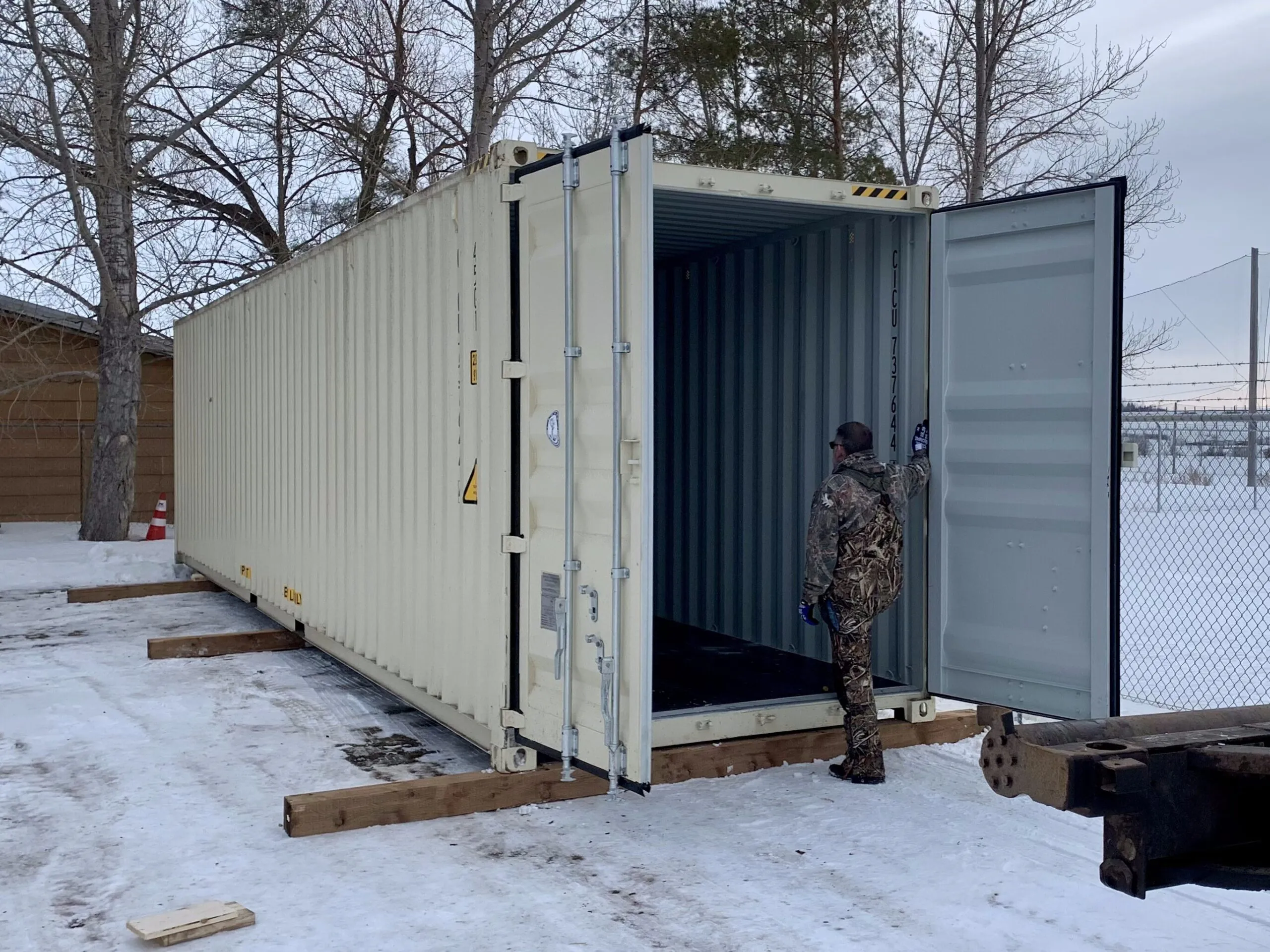 A customer inspecting a 40' High Cube New (One-Trip) Beige shipping container after placement on wood blocks. The container is freshly delivered and in pristine condition, showcasing its durability and quality. StoreCan offers new and used shipping containers for sale across Canada with fast delivery. Get yours today! Call +1 (800) 866-0208 or visit StoreCan.ca